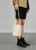 Woman holding a small white lambskin woven leather bucket bag with adjustable strap