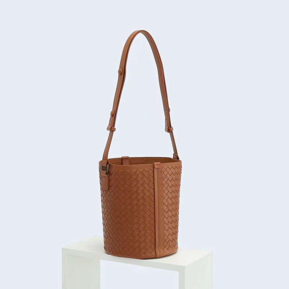 Brown woven lambskin leather bucket bag with adjustable shoulder strap on white stand