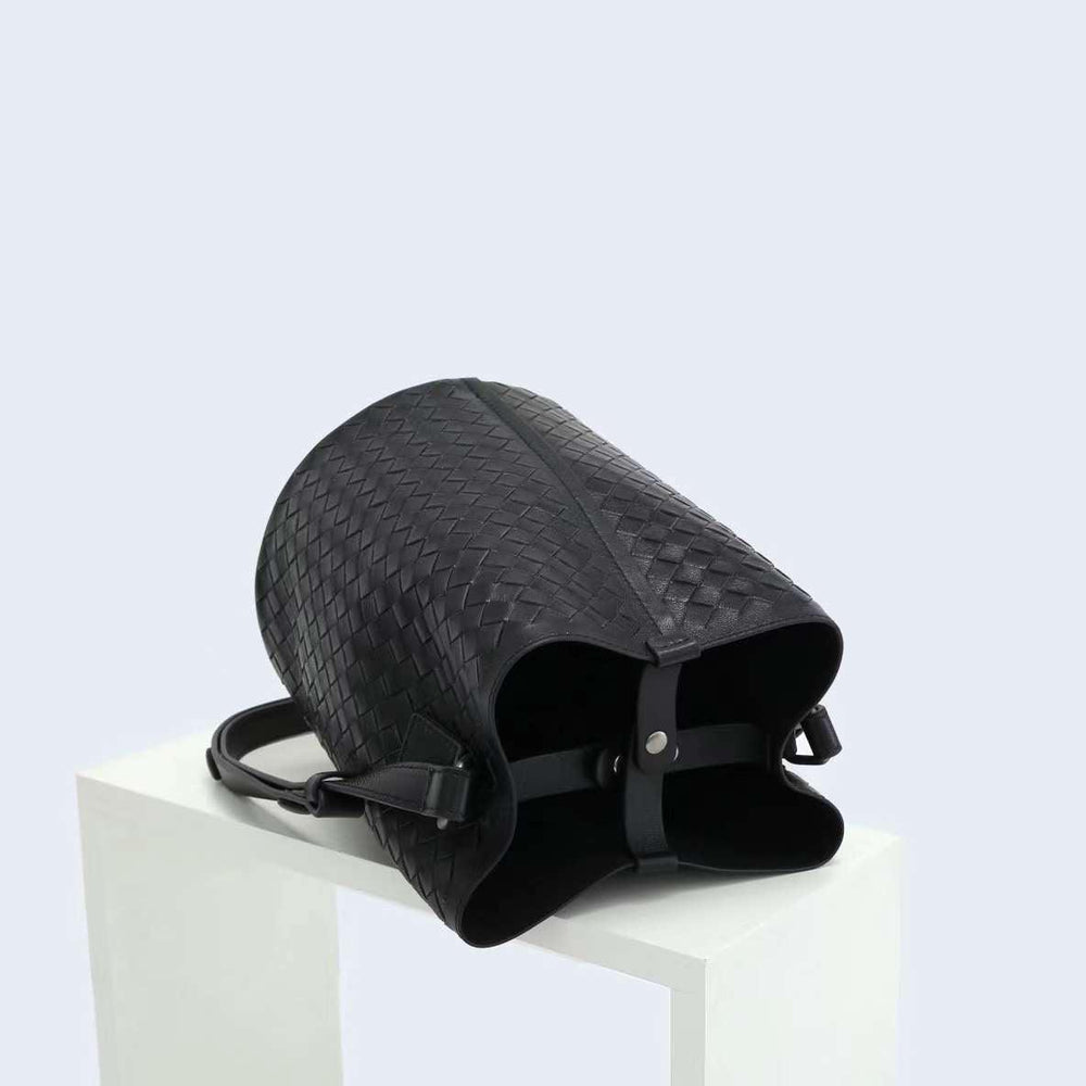 Black woven lambskin leather bucket bag with shoulder strap on white display block
