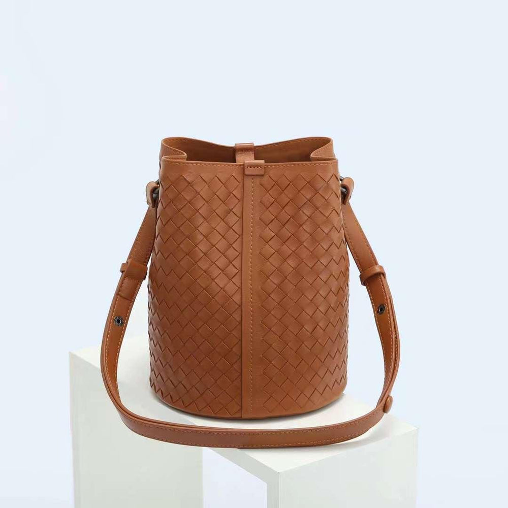 Brown woven leather bucket bag with adjustable shoulder strap on white pedestal