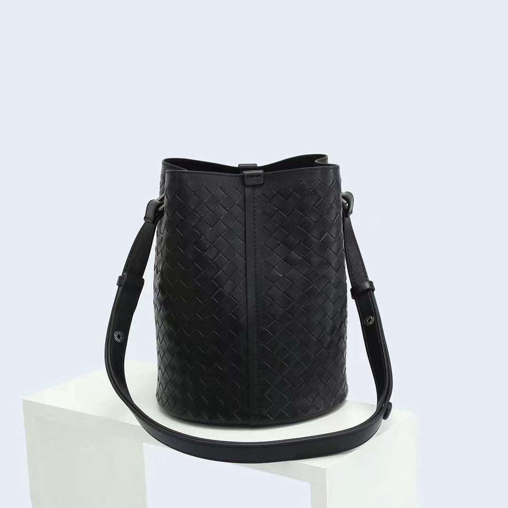 Black woven lambskin leather bucket bag with adjustable shoulder strap on white display
