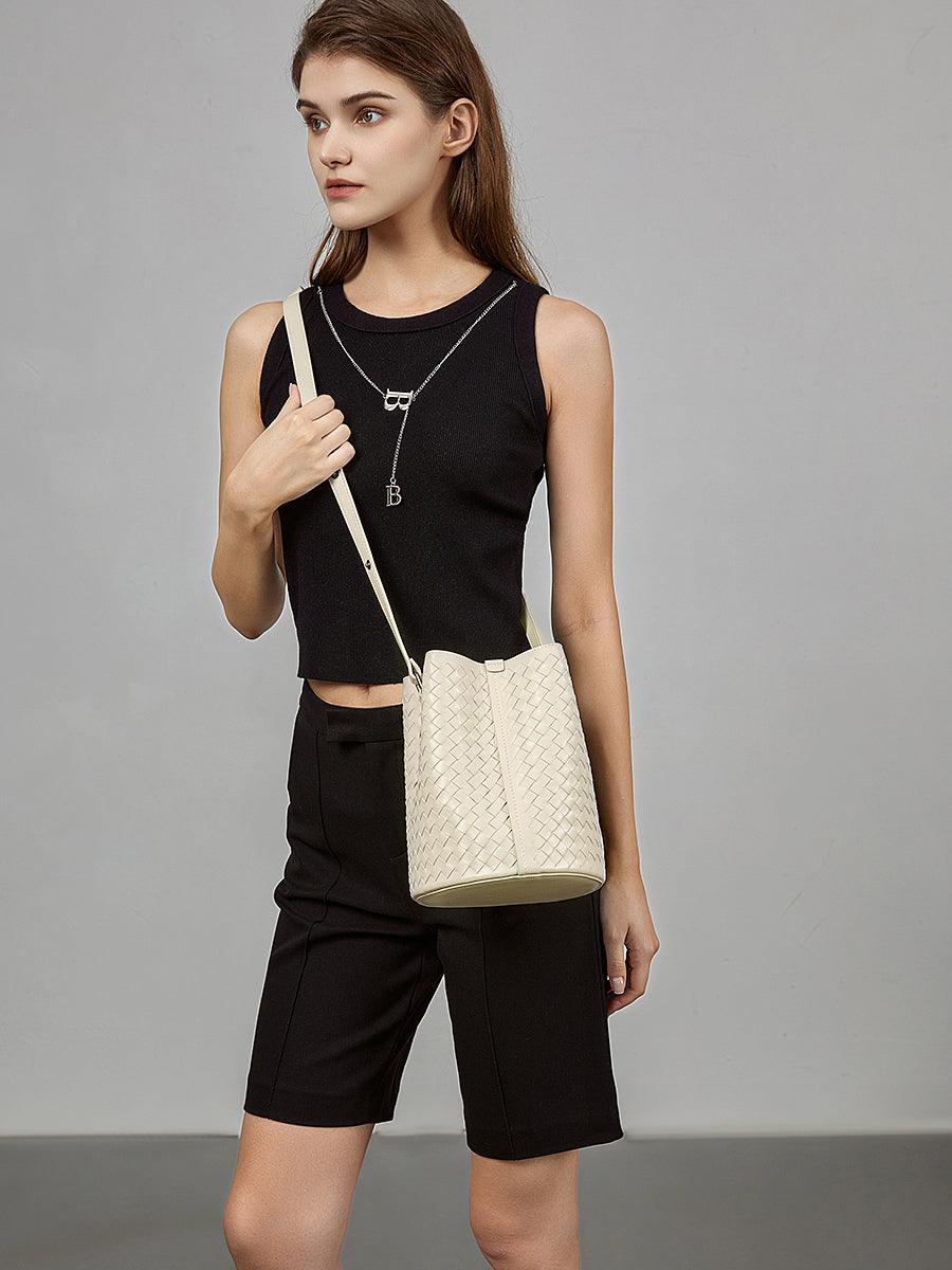 Woman wearing a woven lambskin leather bucket bag crossbody, cream color, minimalist style