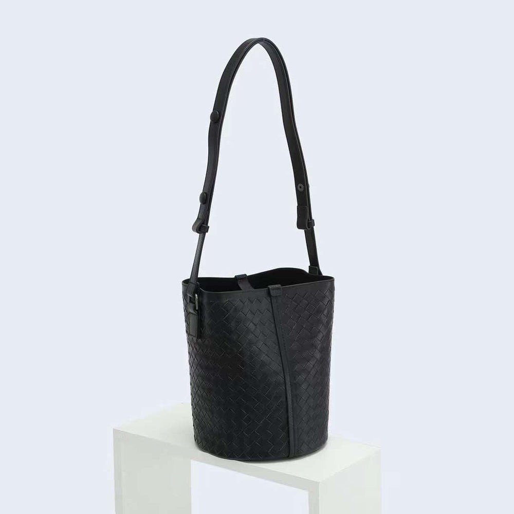 Black woven lambskin leather bucket bag with adjustable shoulder strap on white pedestal