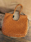 Brown woven cowhide leather summer bag with braided handles on a rustic surface