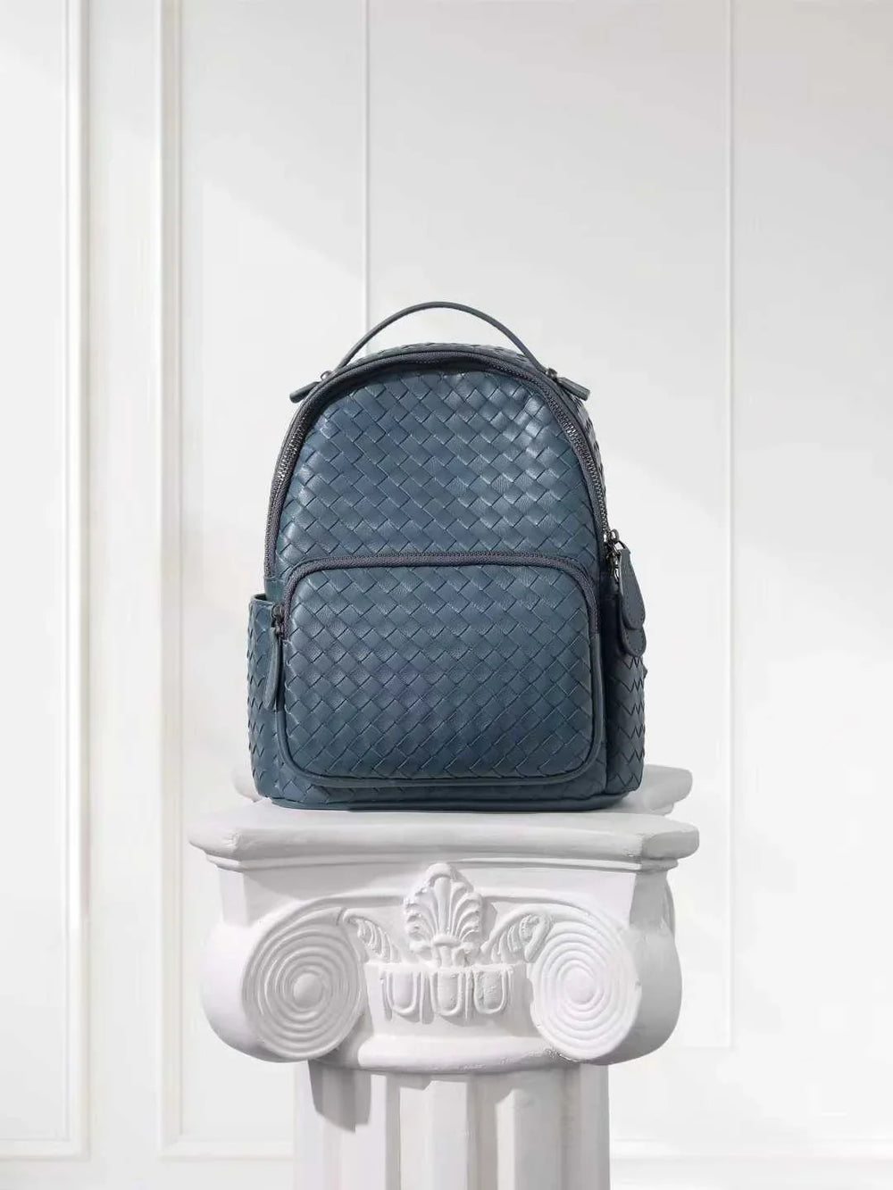 Small blue woven lambskin leather backpack on white pedestal, elegant designer bag
