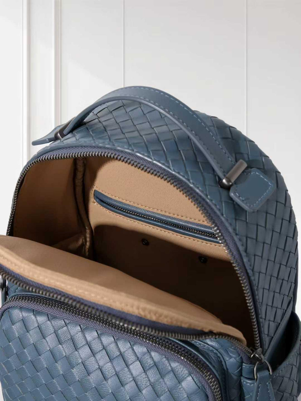 Small blue handwoven lambskin leather backpack with open zipper and tan lining