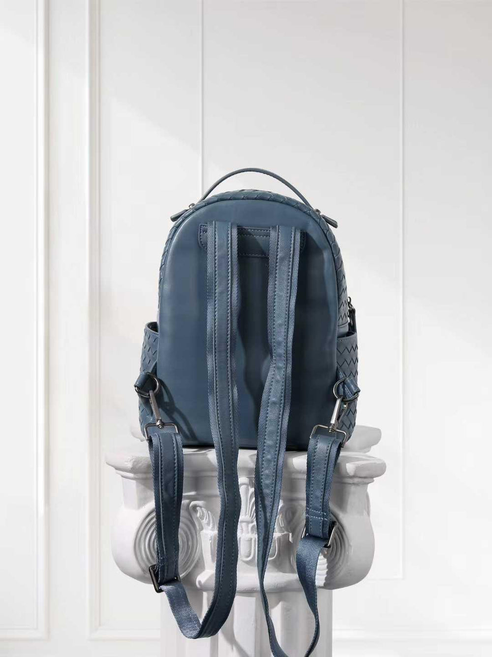 Blue lambskin leather woven backpack with adjustable straps on white pedestal