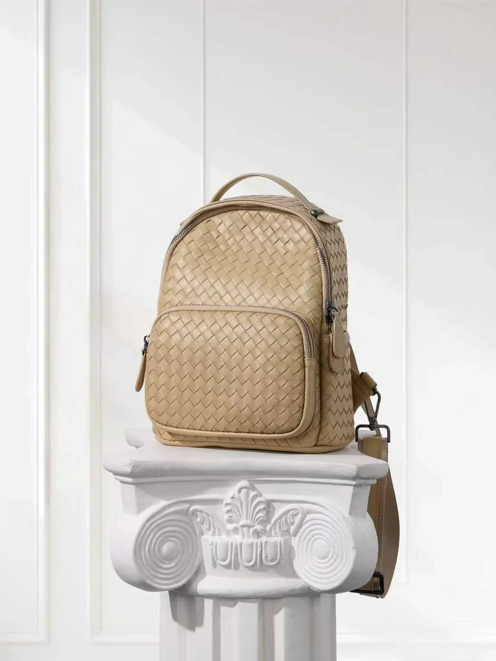Handwoven beige lambskin leather small backpack with front pocket on white column pedestal