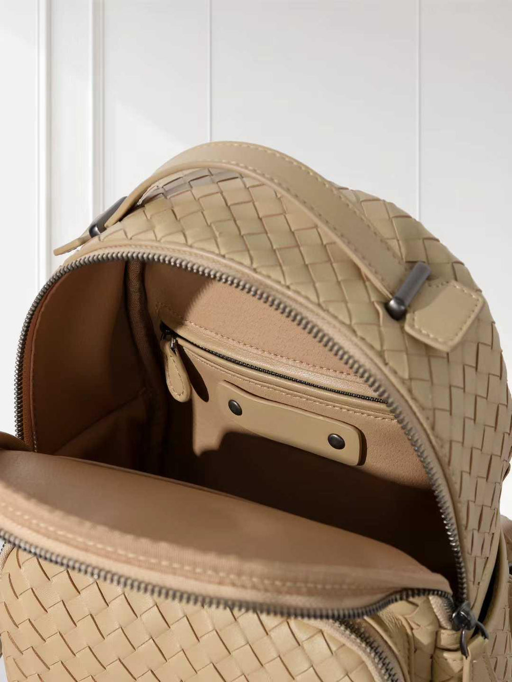 Small beige handwoven lambskin leather backpack with zipper open, showing interior pockets.