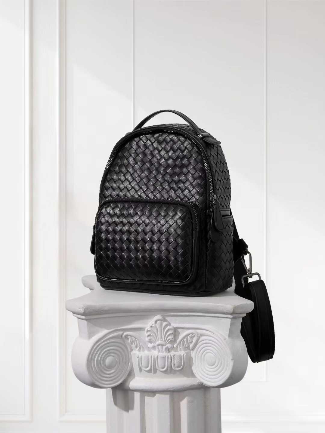 Black handwoven lambskin leather backpack with front pocket on a white decorative pedestal