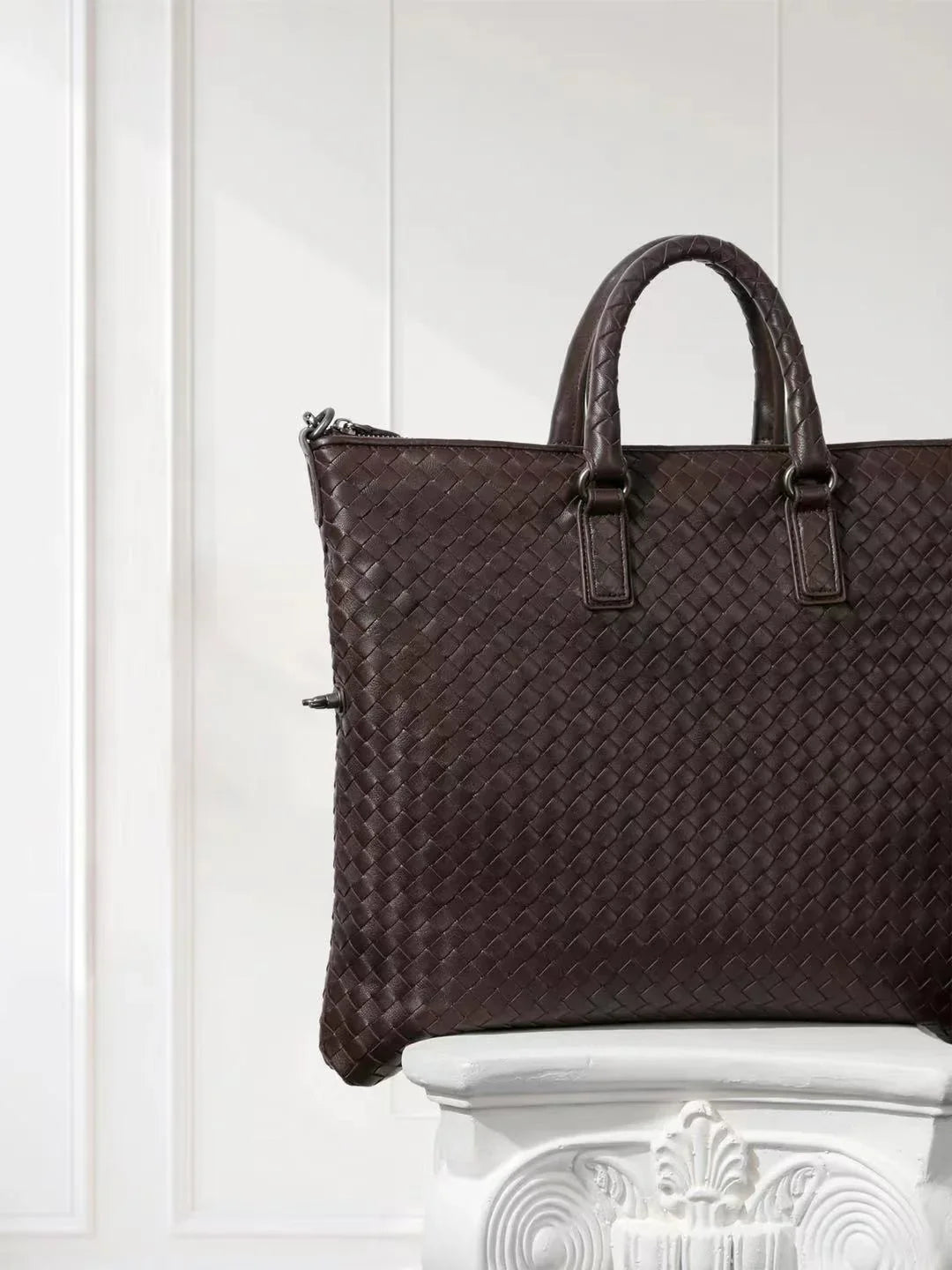 Black intrecciato woven lambskin leather tote bag with top handles, displayed on pedestal