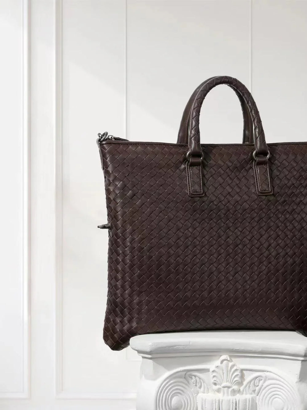Black intrecciato woven lambskin leather tote bag with top handles, displayed on pedestal