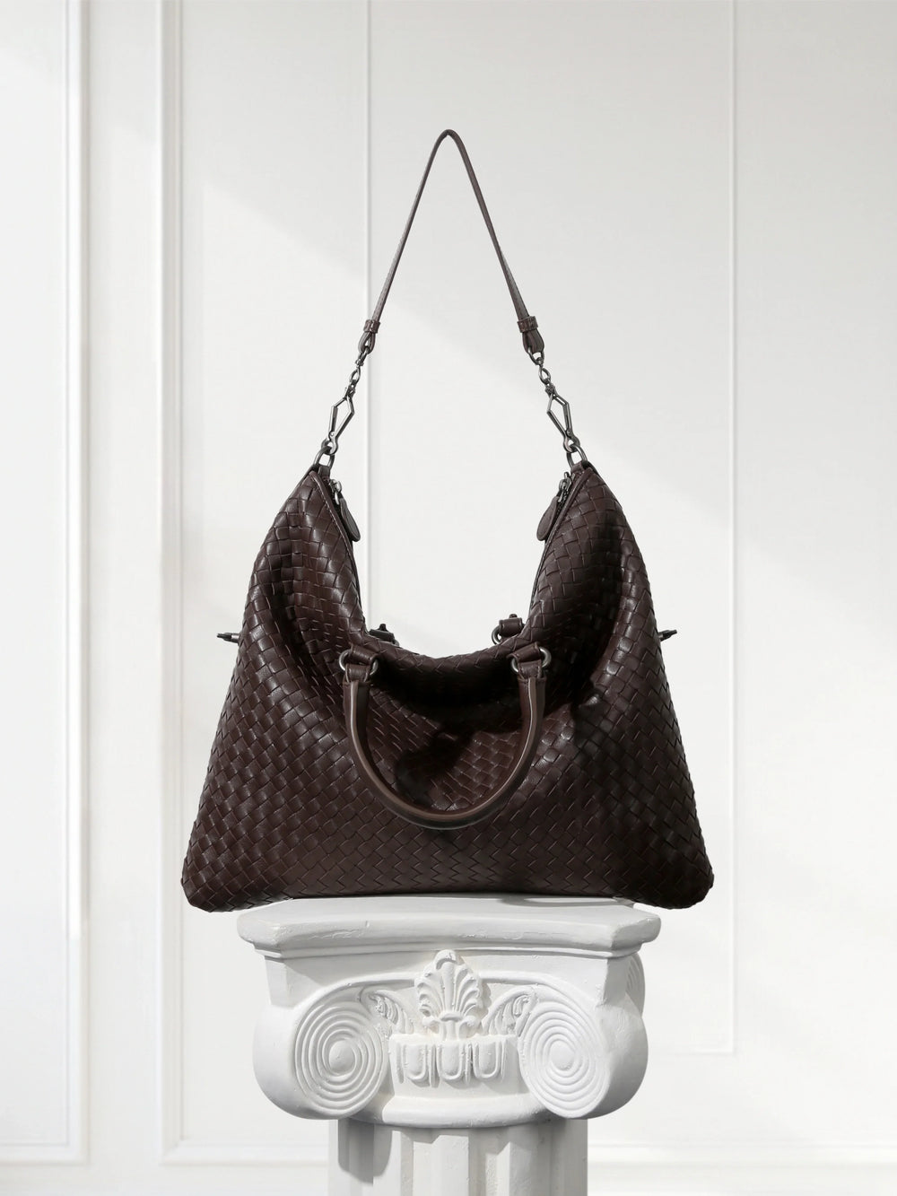 Large black woven lambskin leather tote bag with dual handles and quilted texture, displayed on a white pedestal.
