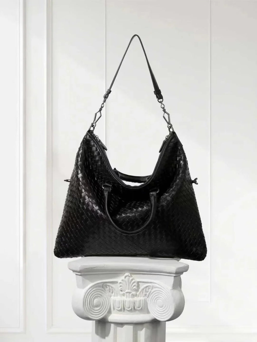 Large black lambskin leather tote with woven intrecciato design on a white pedestal