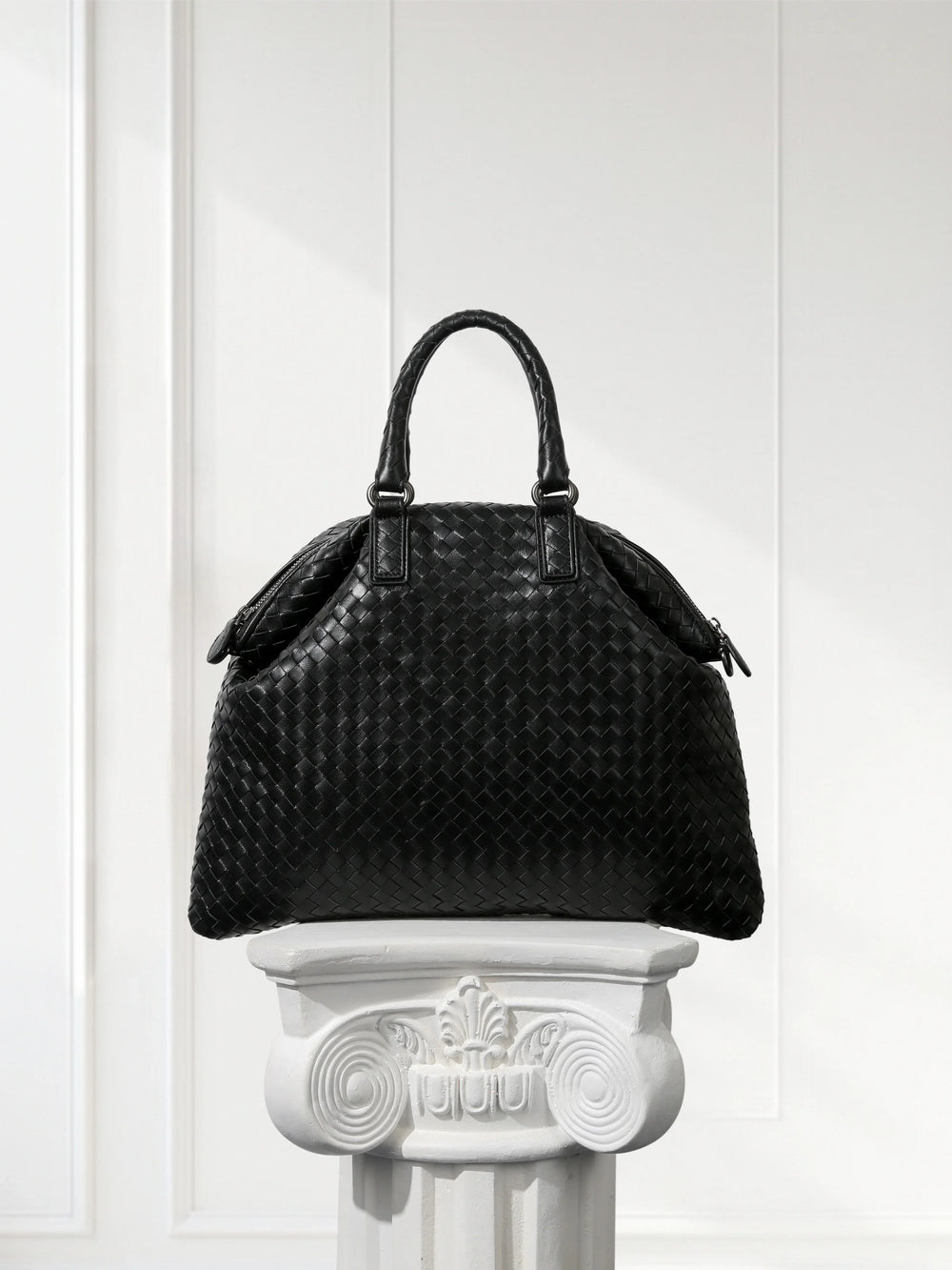 Black intrecciato lambskin leather tote bag with top handles on white pedestal