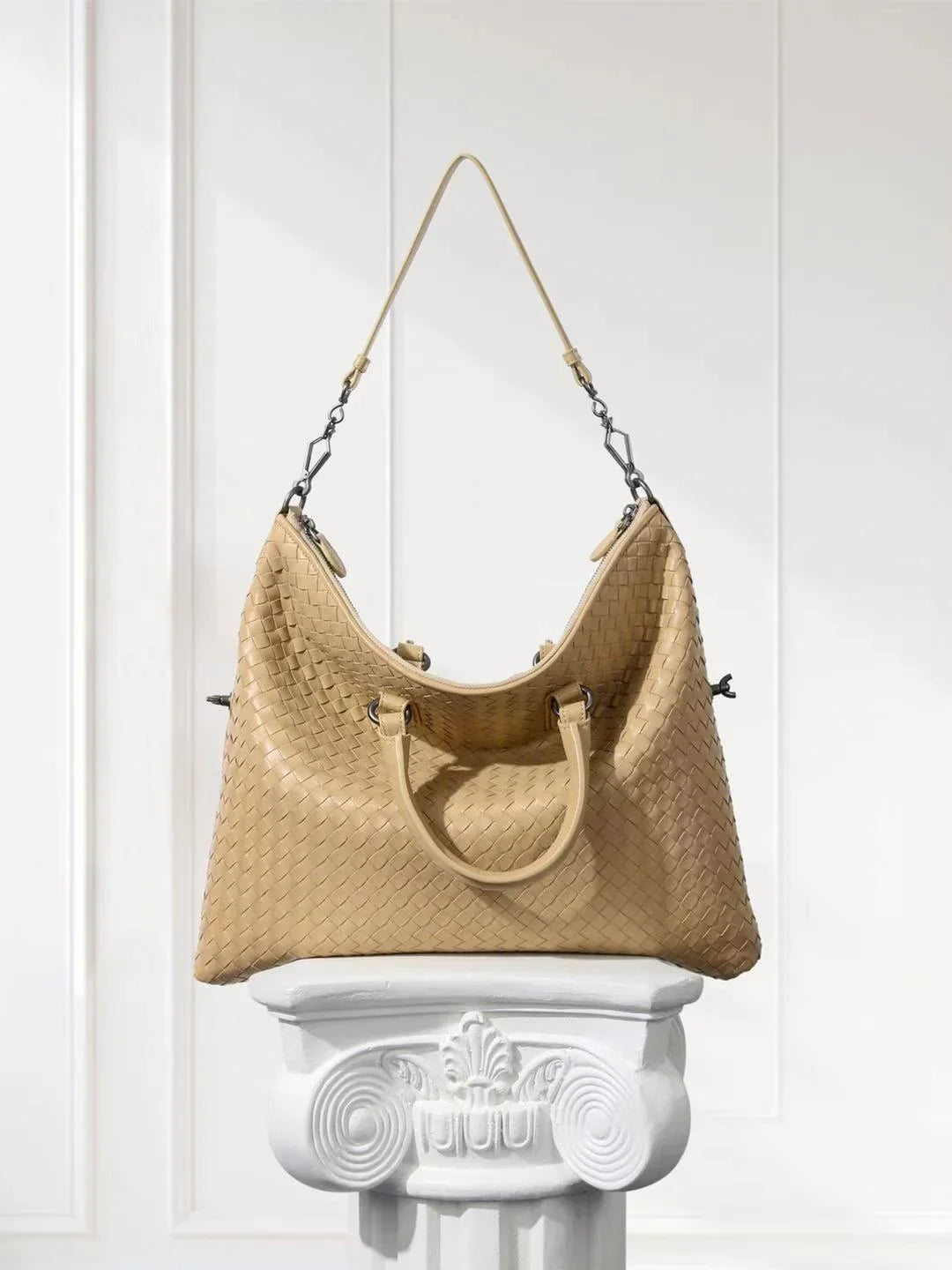 Beige woven leather tote bag with dual handles, displayed on a white pedestal in a bright setting