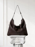 Black woven lambskin leather tote bag with braided design on a white pedestal in bright room