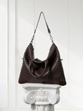 Large black woven lambskin leather tote bag with dual handles and shoulder strap, displayed on a white pedestal.