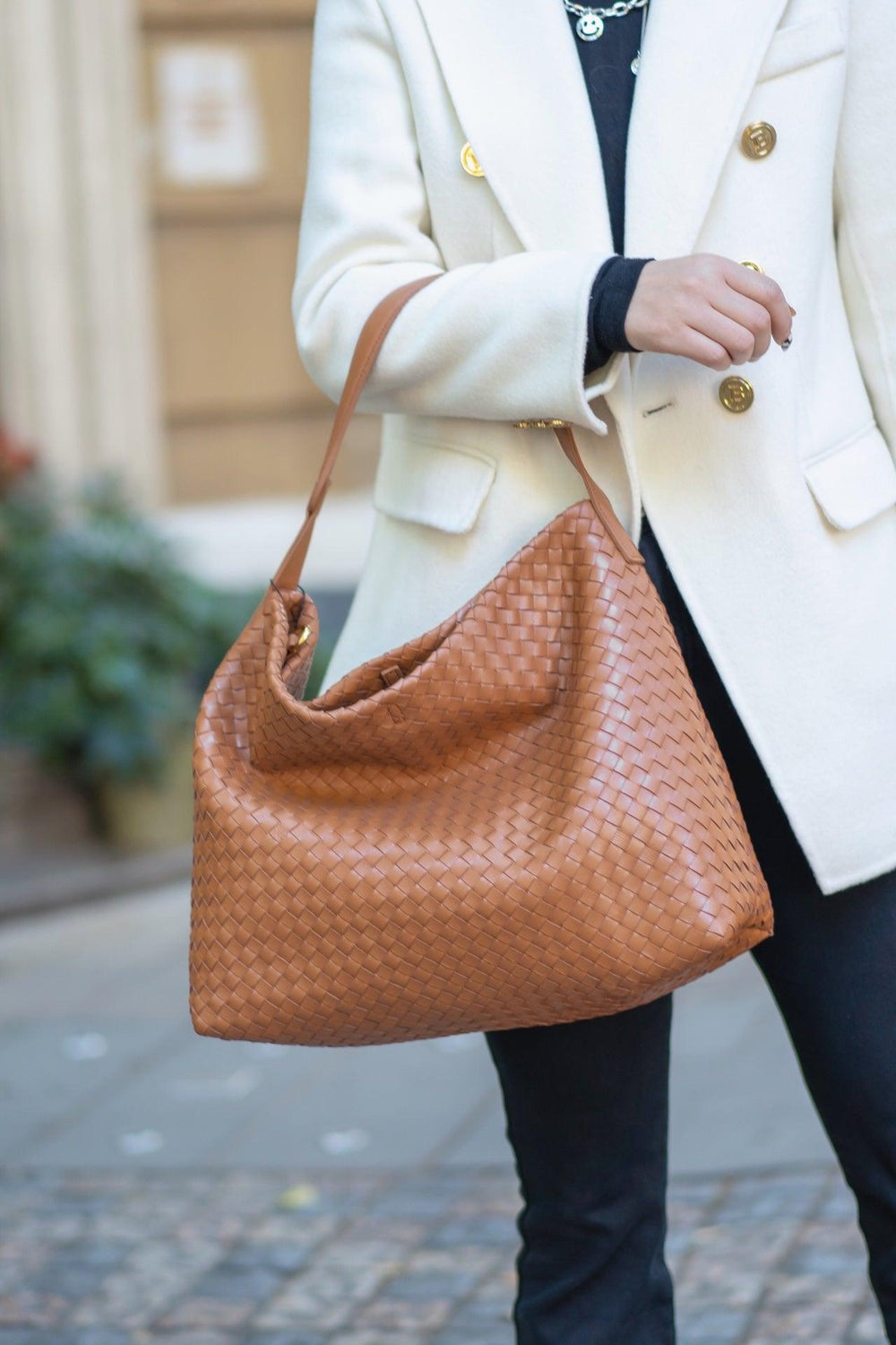 Woman carrying large brown woven lambskin leather shoulder tote bag outdoors