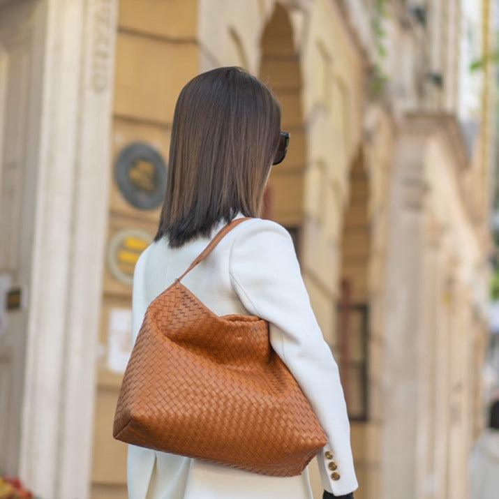 Woman with large brown woven leather tote bag over shoulder, street background