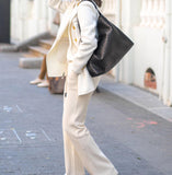 Woman in cream suit carrying large black woven lambskin leather tote bag on shoulder