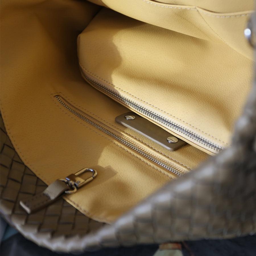 Interior of woven leather tote bag with beige lining and zippered pockets