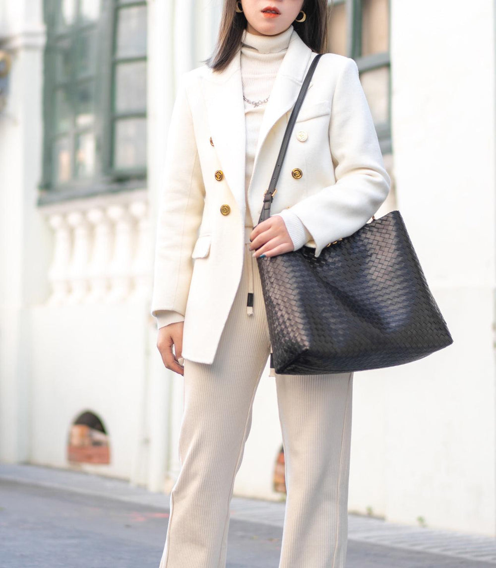 Woman wearing cream outfit holding large black woven leather tote bag on street