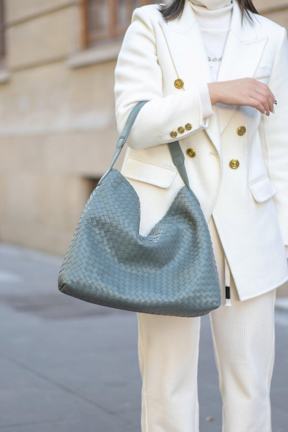 Woman carrying a large gray woven lambskin leather tote bag, styled with a white suit.