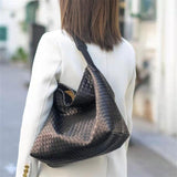 Woman wearing a large black woven leather tote bag on shoulder outdoors