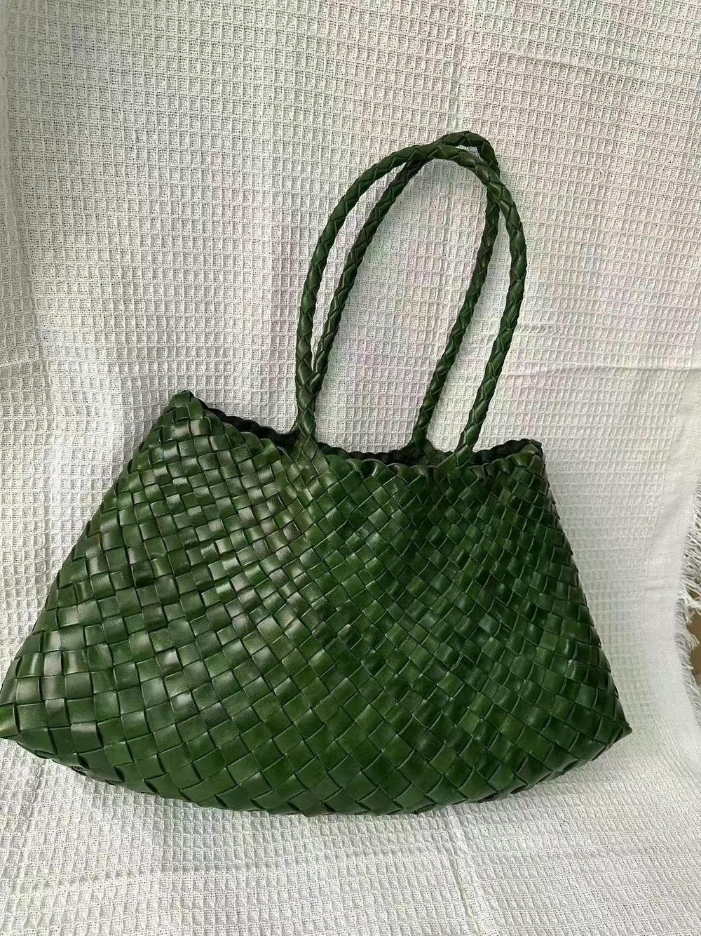 Green woven leather hobo bag with braided handles on a textured white background