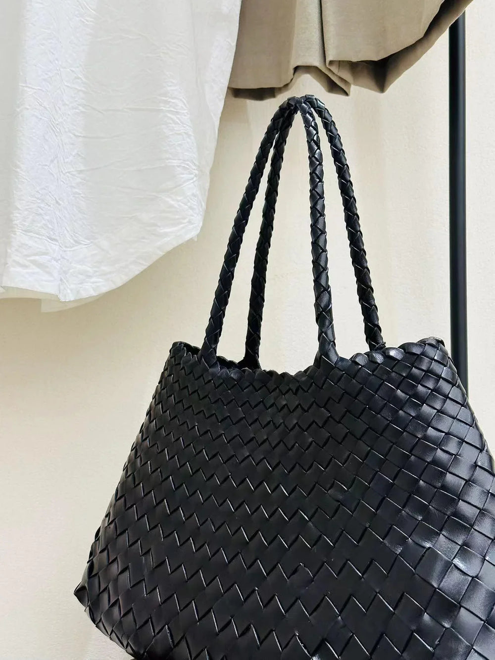 Black woven leather hobo bag with double braided handles, hanging indoors on a rack.