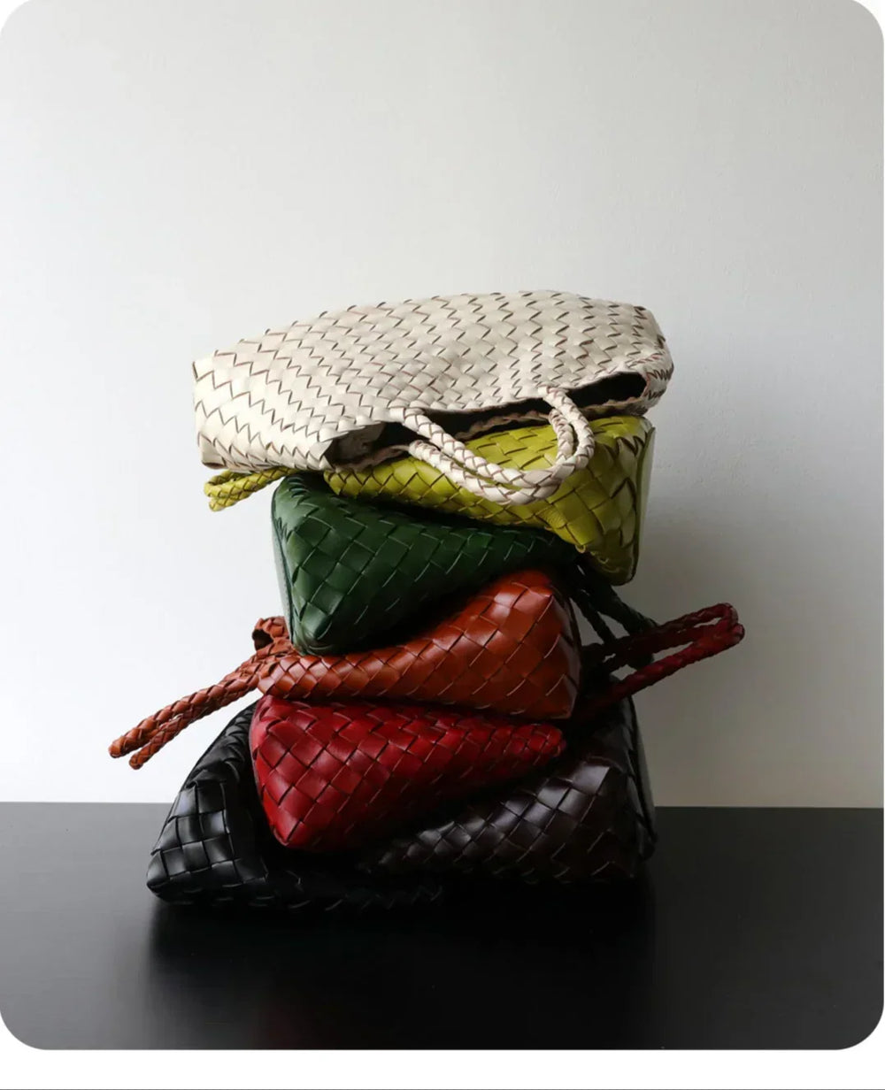 Stack of woven leather hobo shoulder bags in assorted colors on a black surface