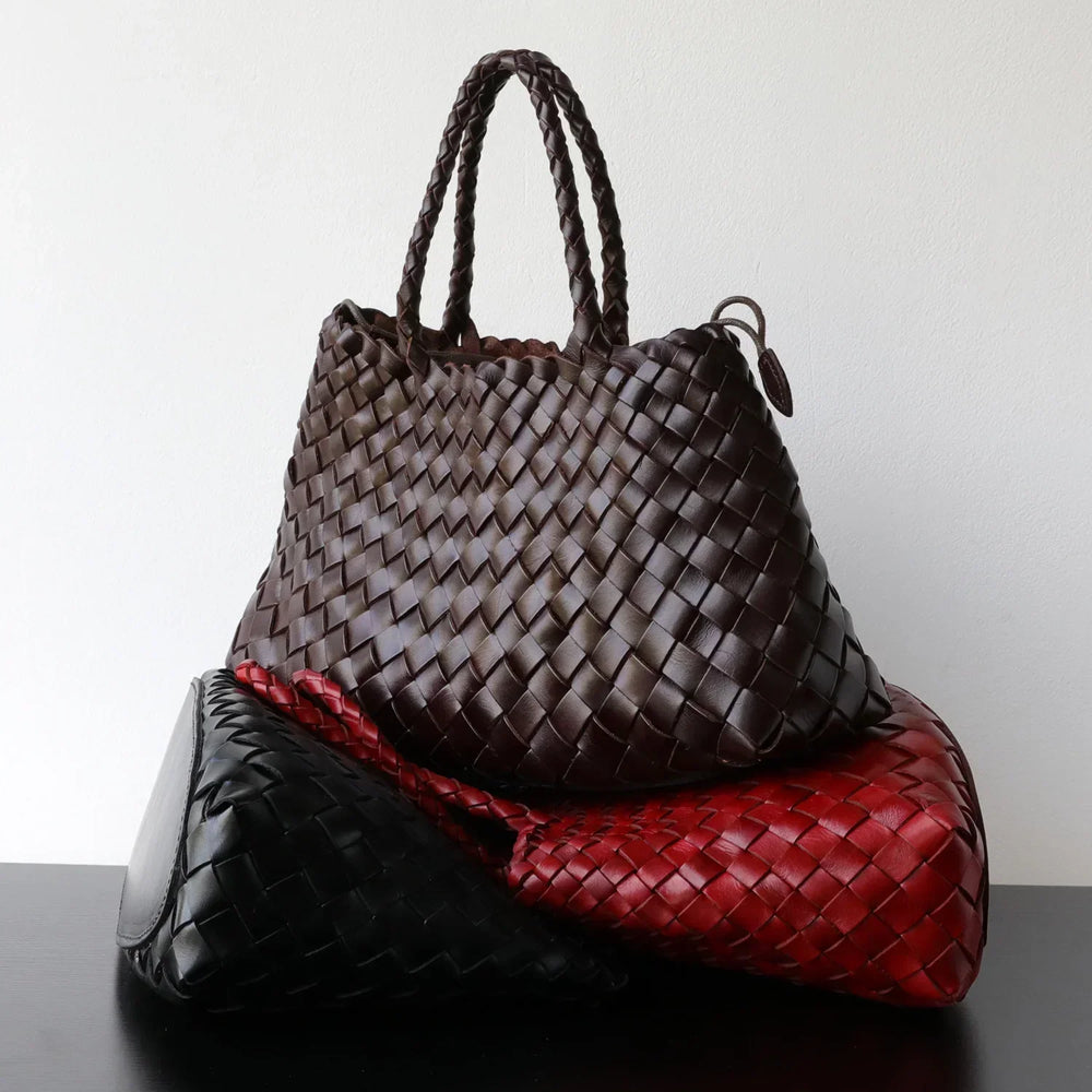 Stack of woven leather handbags in brown, red, and black with braided handles