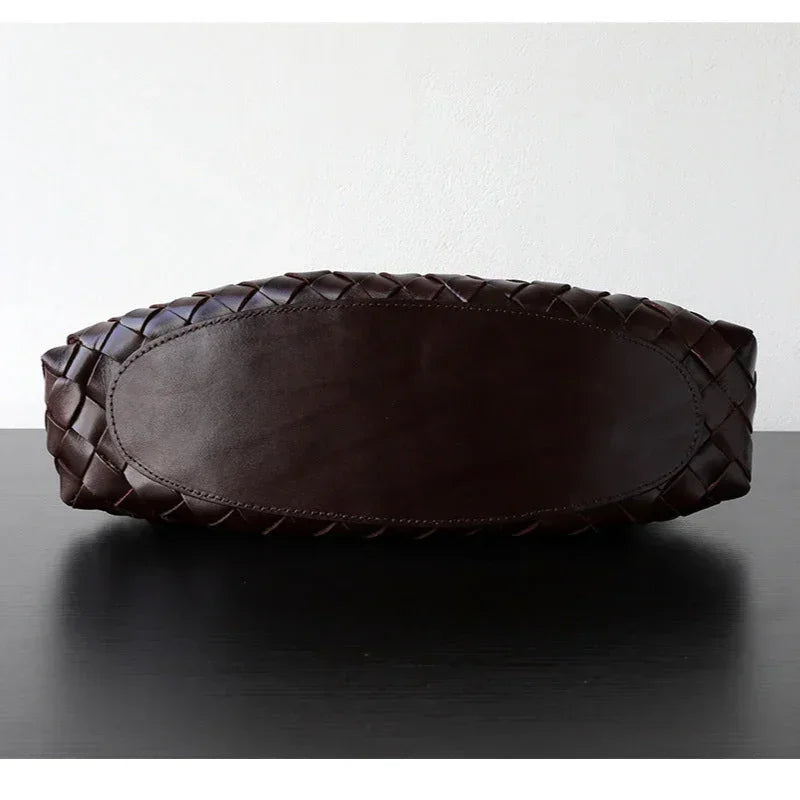 Bottom view of a dark brown full grain leather woven shoulder bag on a black table