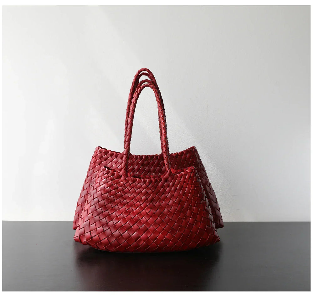 Red woven leather hobo shoulder bag with long handles on a dark table, trapezoidal shape