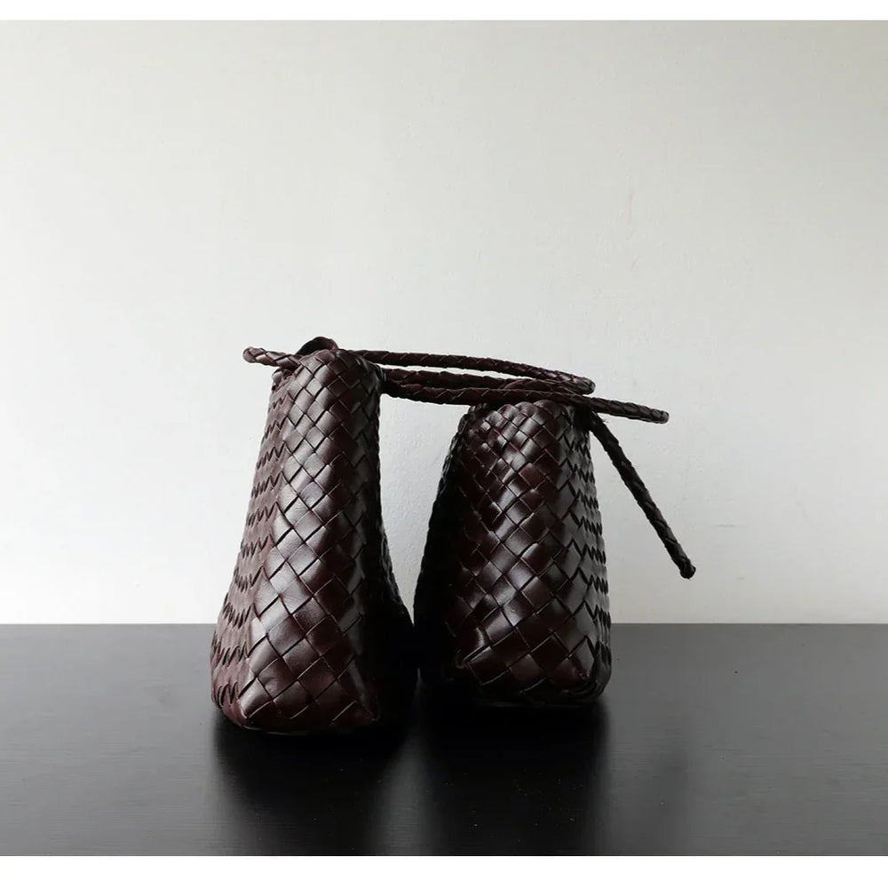 Side view of two dark brown woven leather hobo bags with long handles on black surface