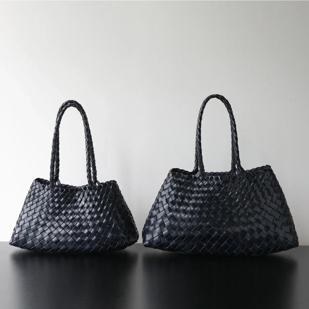 Two black woven leather hobo shoulder bags with long handles on a black surface