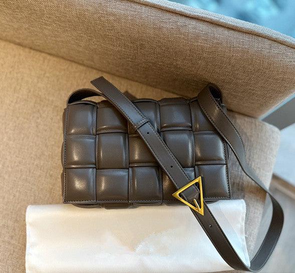 Small quilted lambskin leather shoulder bag with handwoven design and gold buckle on beige sofa