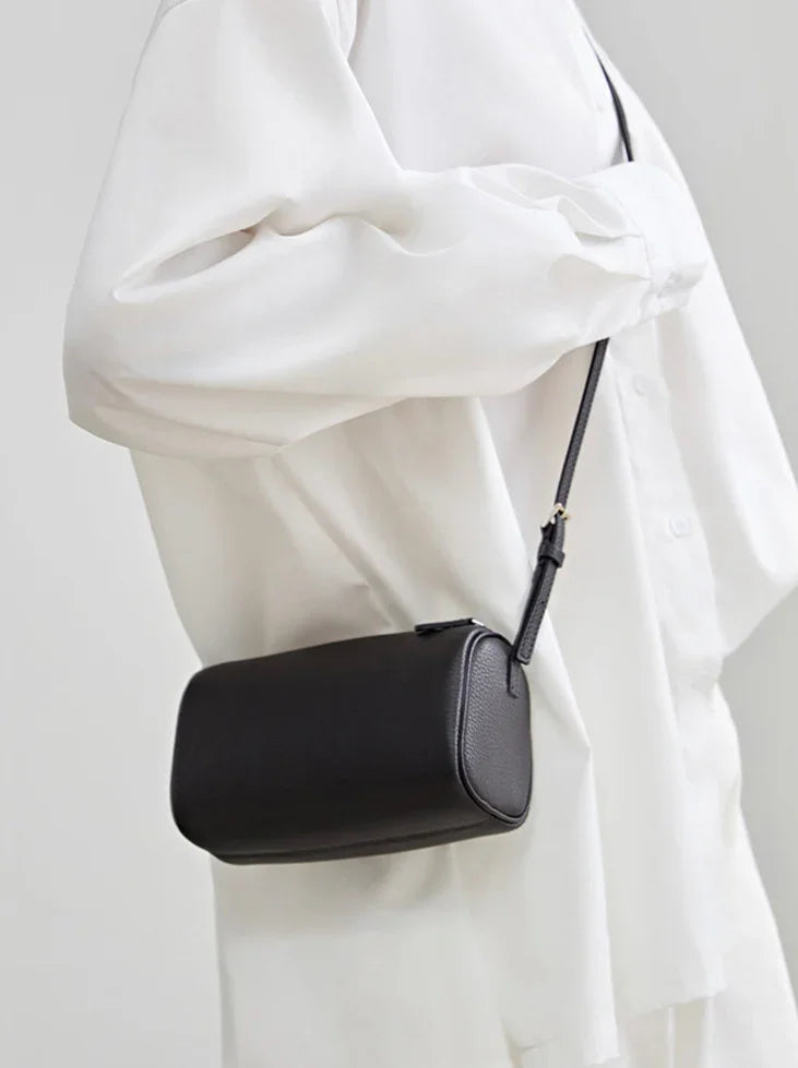 Minimalist black leather mini box bag with crossbody strap, worn over a white shirt