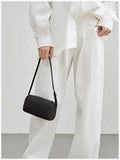 Woman in white outfit holding a black lambskin leather mini Boston bag with top handle