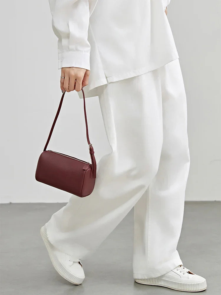 Woman in white outfit holding a minimalist burgundy lambskin leather mini Boston bag