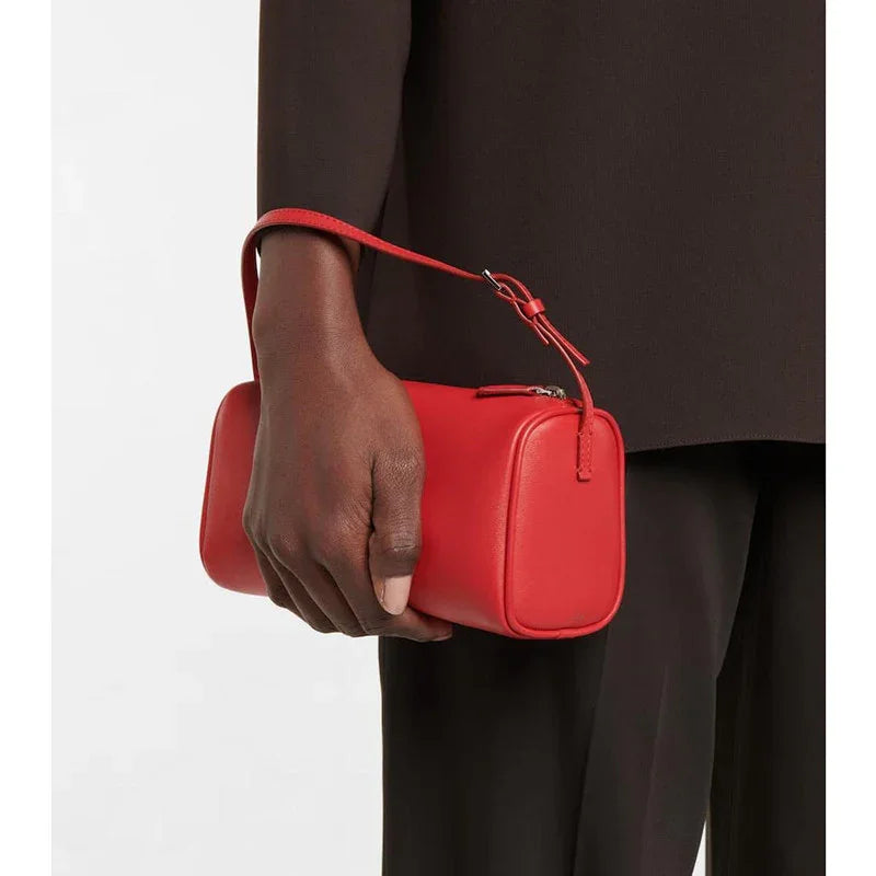 Person holding a small red lambskin leather box bag with wrist strap, minimalist handbag style