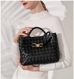 Black lambskin woven leather shoulder bag with gold metal buckle, held by woman in white sweater