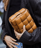 Woman holding a brown lambskin leather quilted shoulder bag with handwoven design