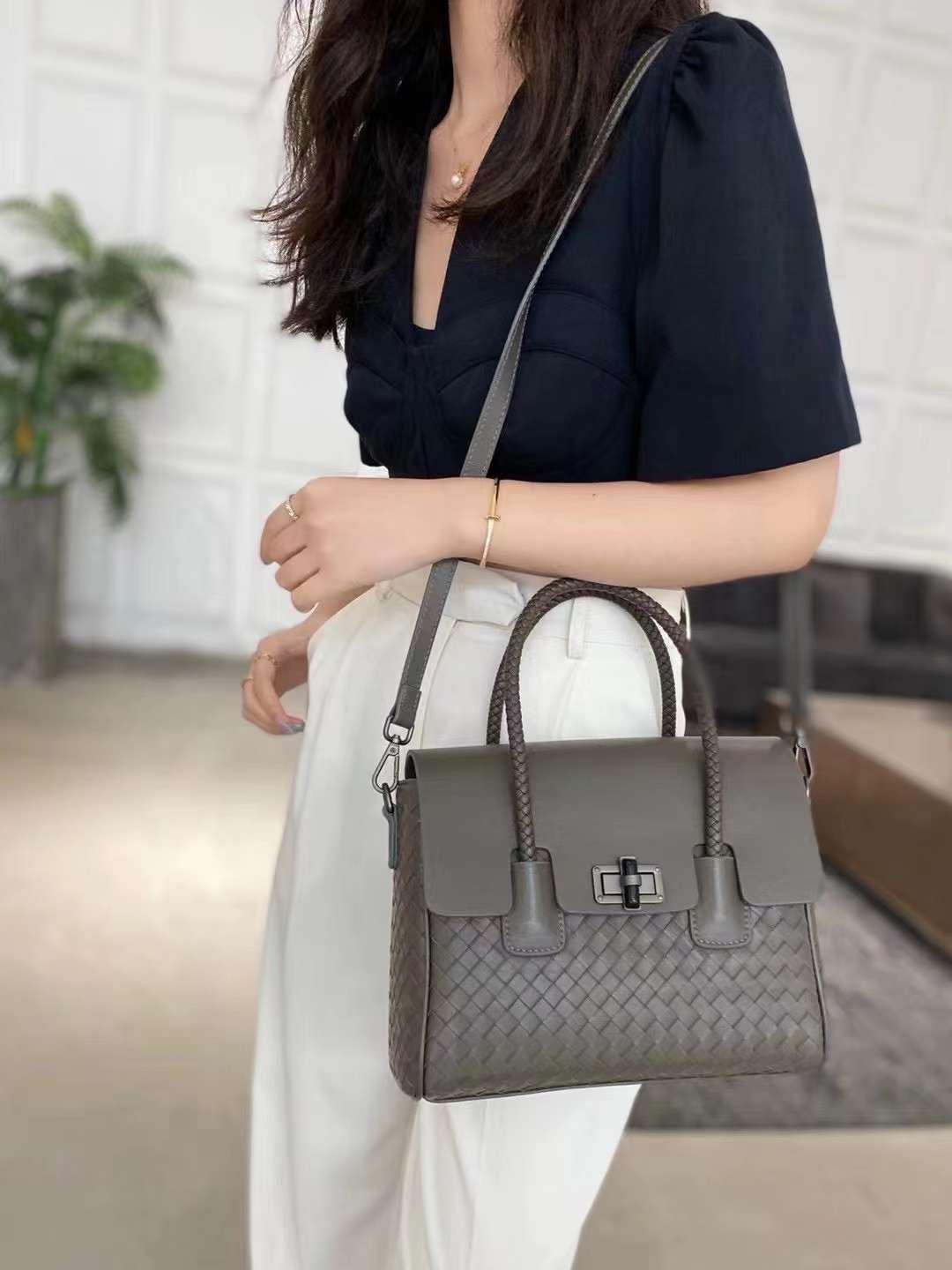 Woman holding a small woven lambskin leather shoulder bag with top handle and crossbody strap