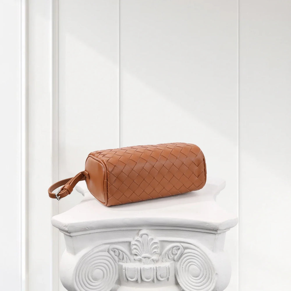 Tan woven lambskin leather Boston bag with wrist strap on ornate white pedestal