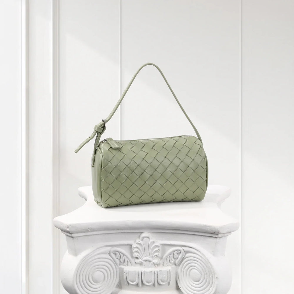 Sage green lambskin leather woven mini shoulder bag with top handle on white pedestal