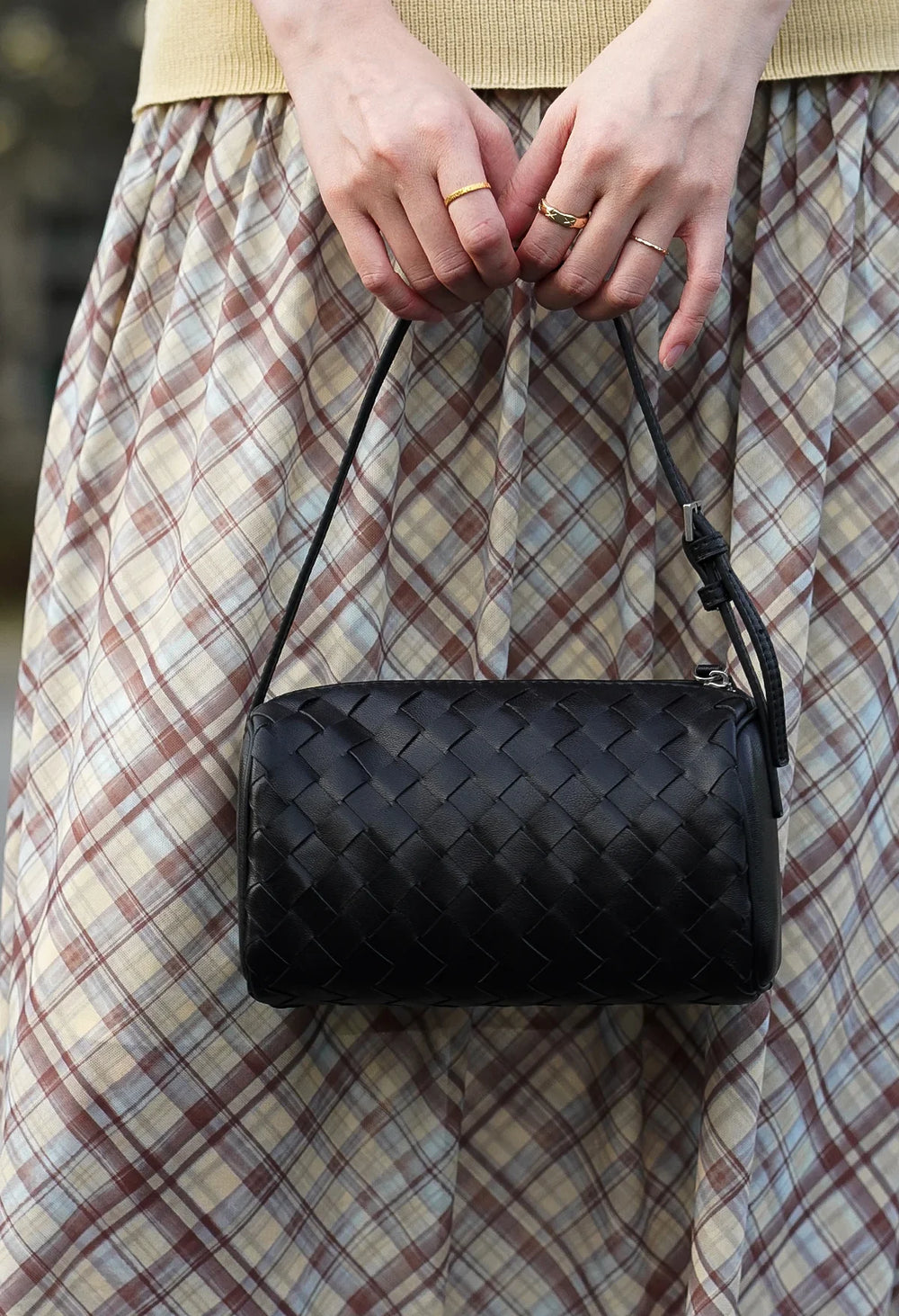 Woman holding a black woven lambskin leather mini Boston bag with shoulder strap