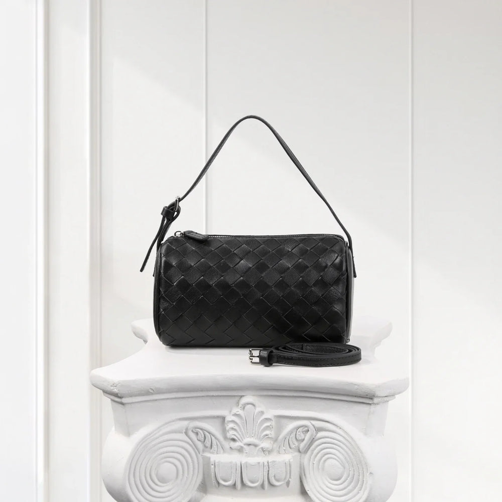 Black woven lambskin leather Boston bag with shoulder strap on elegant white pedestal