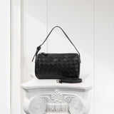 Black woven lambskin leather Boston bag with shoulder strap on elegant white pedestal